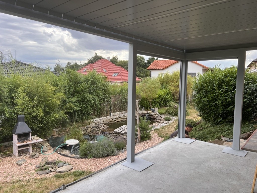 Pergola na terasu zespodu: lamelová střecha a světle šedé sloupky na patkách